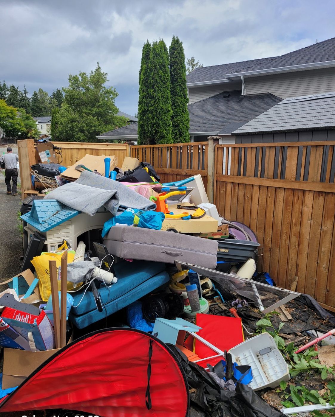 A large mound of household junk, furniture and toys heaped against a Nanaimo fence during a property clearing